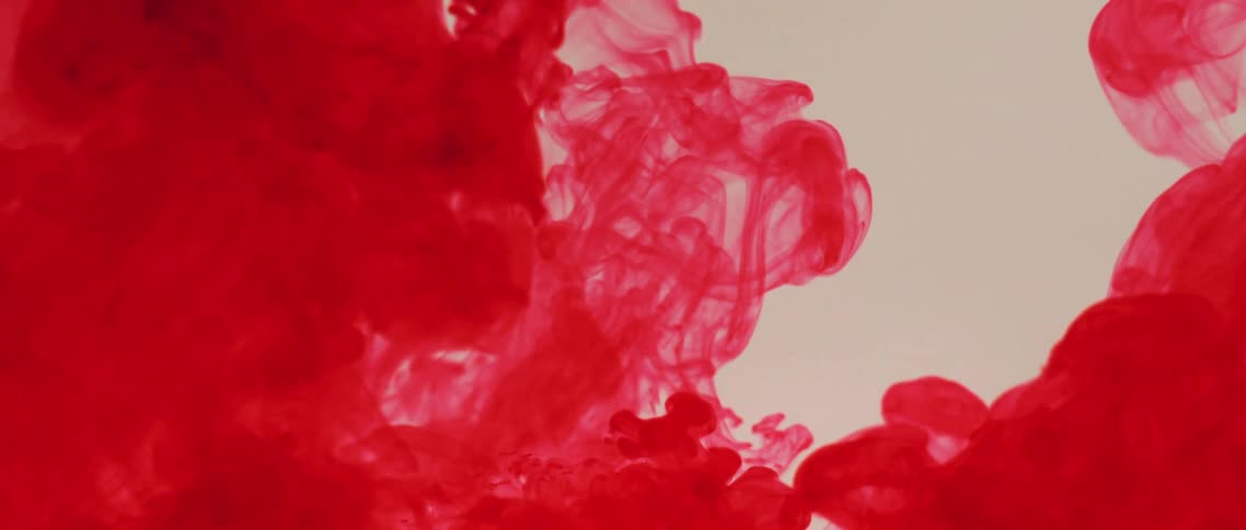 Bright red ink swirling and flowing up a tank filled with clear water