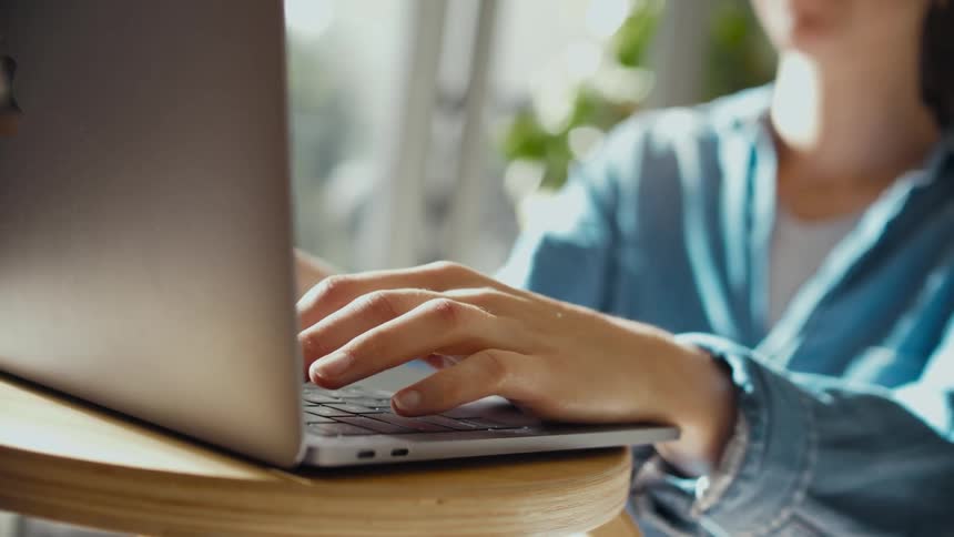 A person typing on a laptop while sitting at a wood table