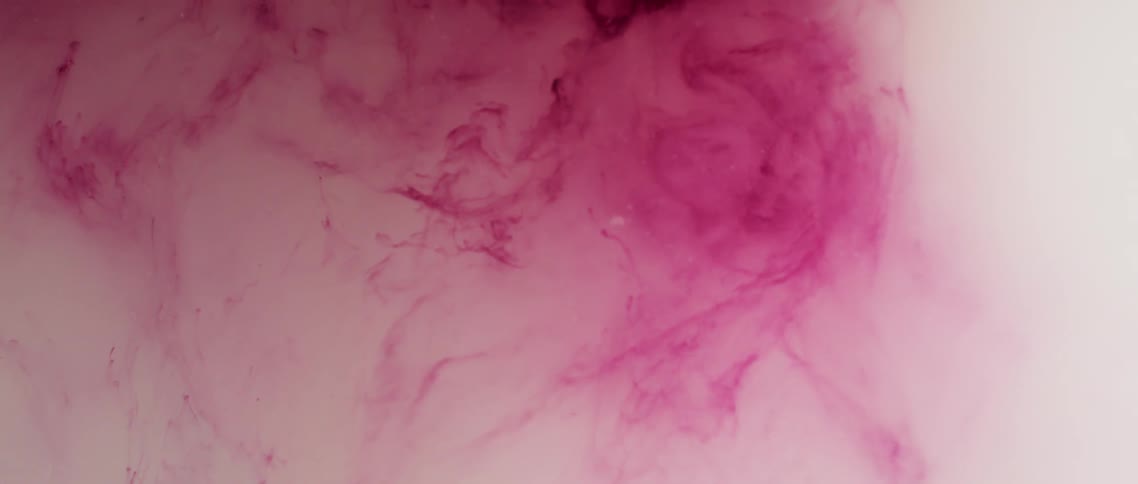 Pink ink spreads and swirls on the white surface