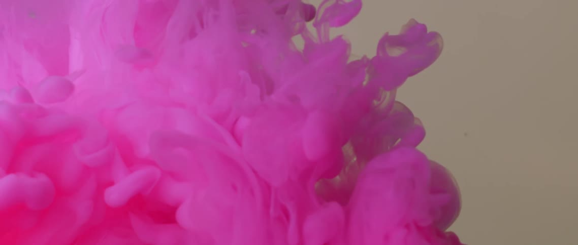 Pink powder dye bursts and flows as it expands in liquid