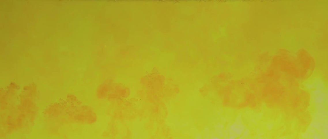 Orange clouds of dye burst upwards in yellow liquid