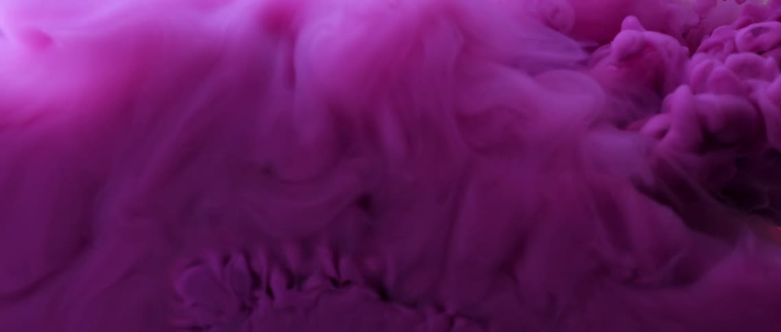 Bright purple ink floating in waves inside a tank of clear water