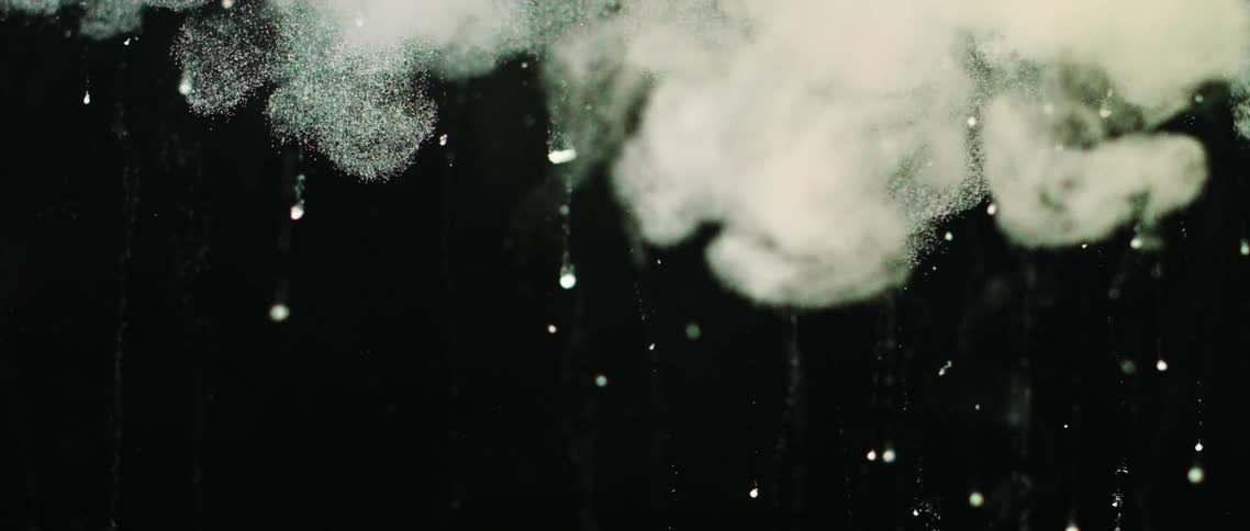 White clouds and specks of white ink flowing down a water tank on a black background