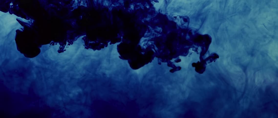 Navy blue dye floats and expands in a blue cloud of liquid