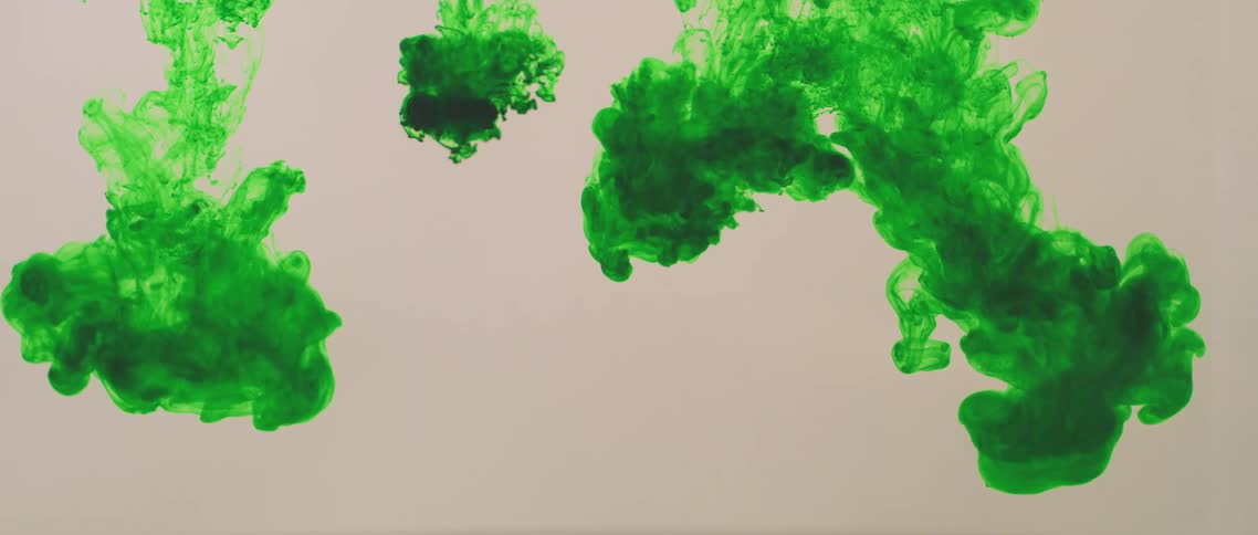 Blobs of bright green ink floating down inside a clear water tank