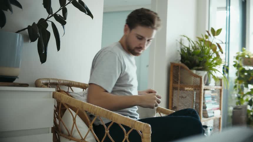Young man sitting on a chair in the living room stands up and enters a room