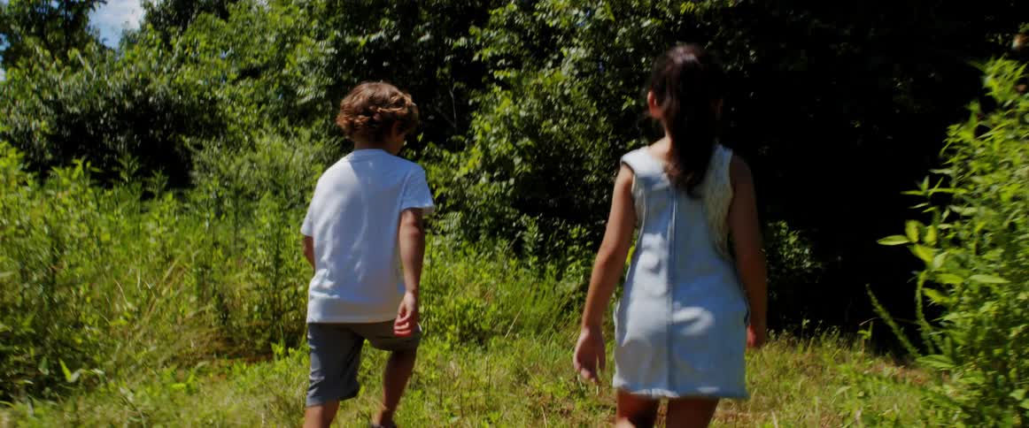 A boy and a girl walking into a forest in a clear sunny day