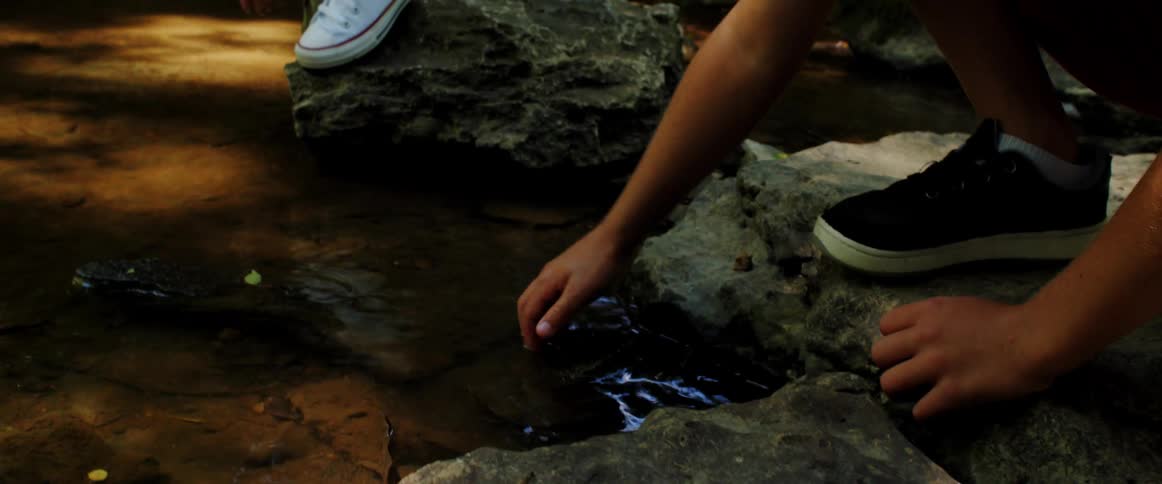 Young child puts his hand in the stream then wipes it on a rock