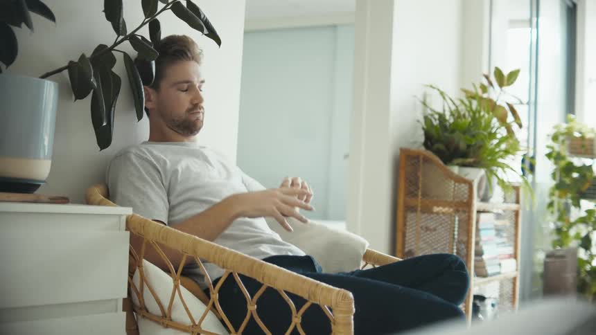 A man puts down his smartphone and tries to relax while sitting in a wicker chair