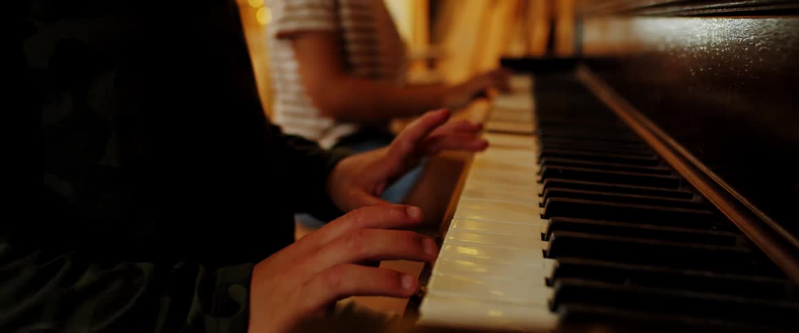 Two children sit on a bench and play the piano