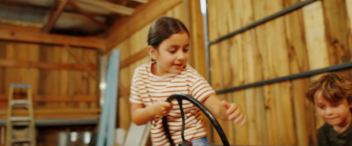 Young boy and girl climb onto a red tractor in the barn