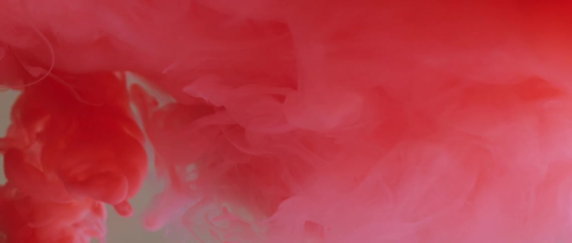 A red and pink liquid gradually spreads around in another liquid to create a cloudy suspension