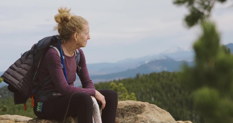 Blonde woman backpacking on a trail in the mountains sitting on a rock looking at the horizon