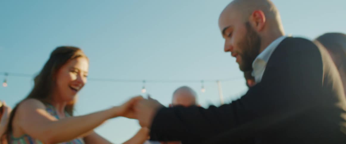 A couple swing dances under string lights at an outdoor reception as friends watch