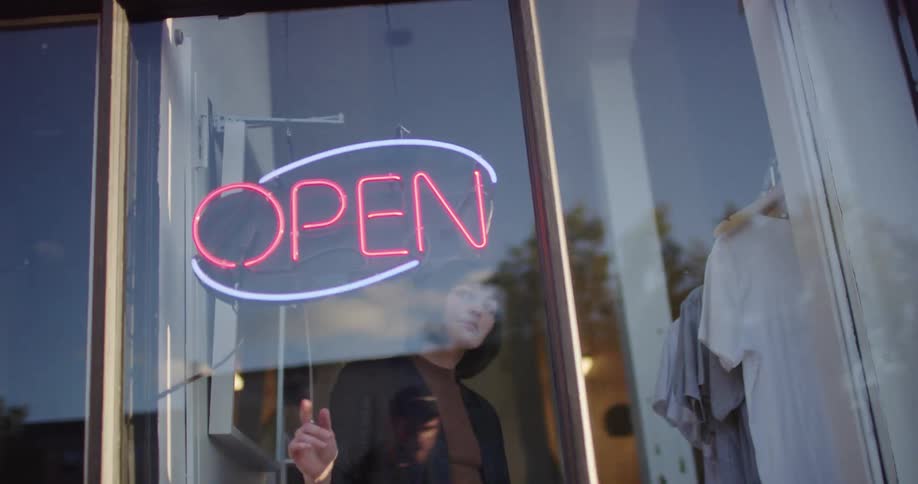 Woman turns the open sign on in a business