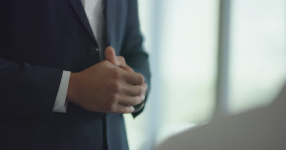 A black man in a suit stands in an office and gestures with his hands