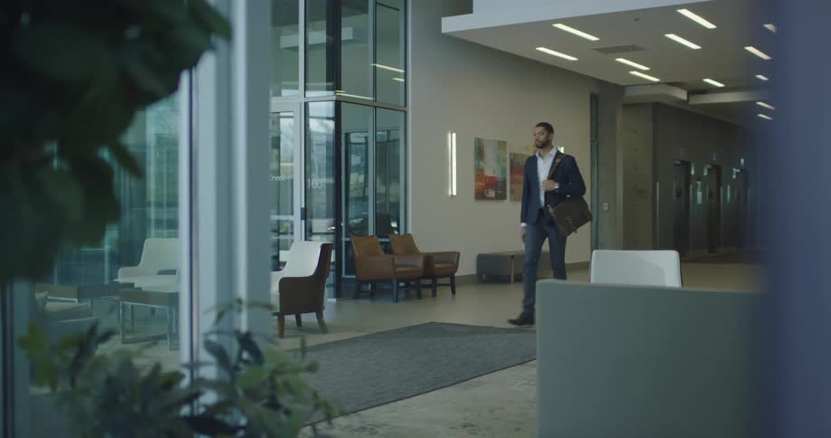 Businessman wearing suit is walking towards the exit of an office building and stops to check cell phone