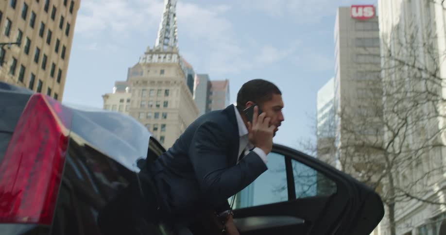 A businessman gets out of a car while talking on the phone