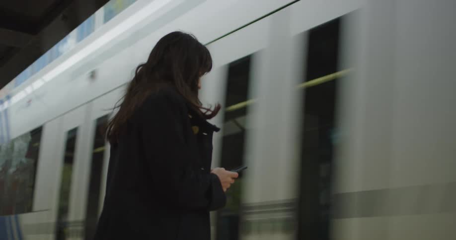 A woman waits at a train station in a city