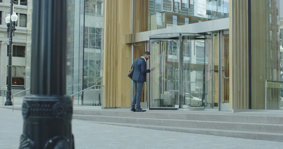 A man talking on his phone walks towards an office building and hangs up as he enters