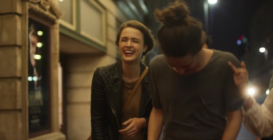 Several laughing men and woman walk a city sidewalk at night