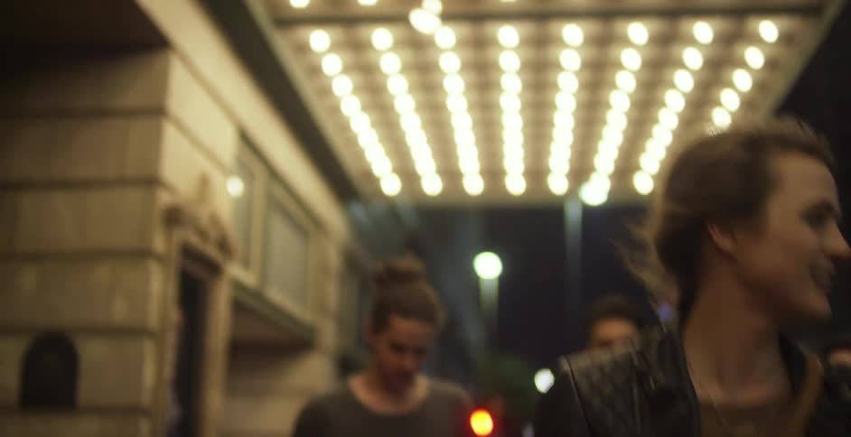 A group of people walk on a city sidewalk at night