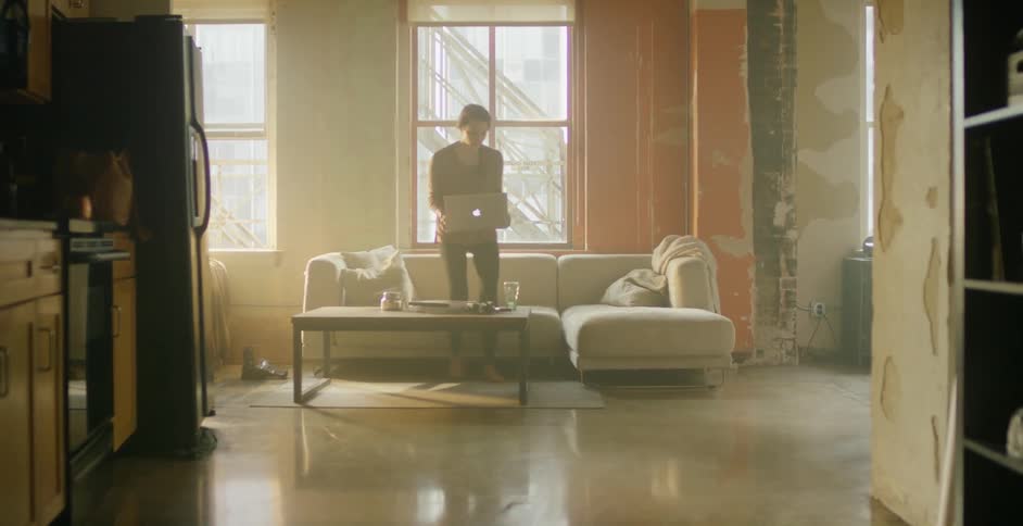 A woman sits down on a couch with a laptop in hand