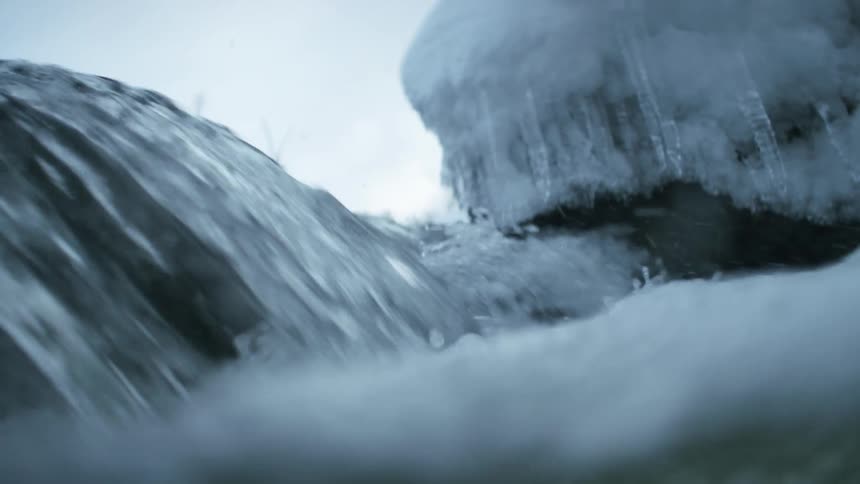 Water from a stream flowing near icicles at winter