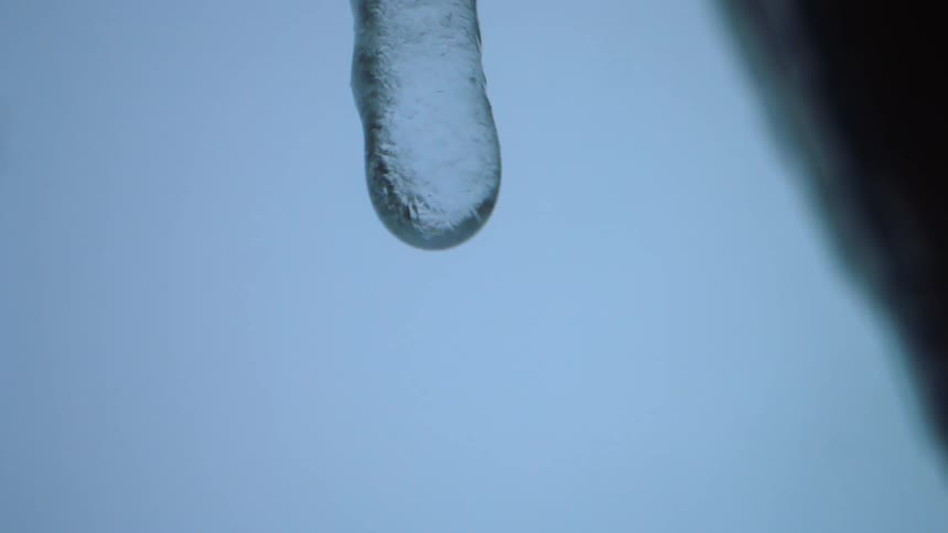 Water dripping from an icicle hanging against blue sky
