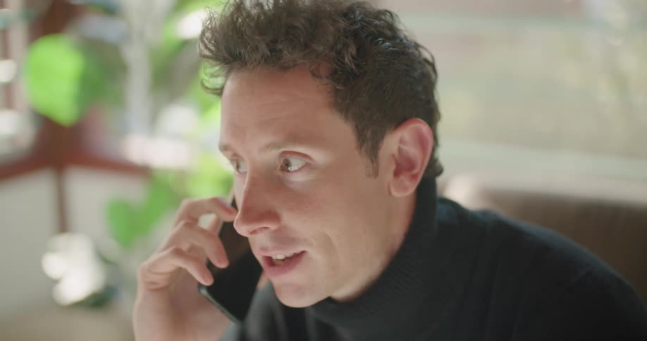 A man with curly hair has a lively conversation while holding is smart phone to his ear