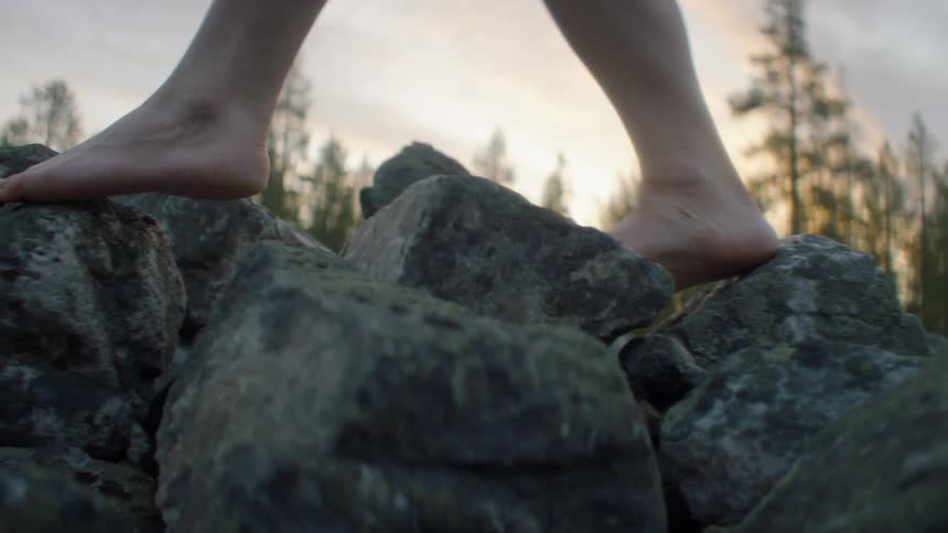 A barefoot person carefully walks across a pile of stones during the day