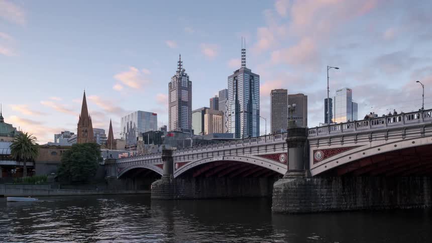 Traffic travels both along and beneath a bridge spanning a river in a metropolis as the sun sets
