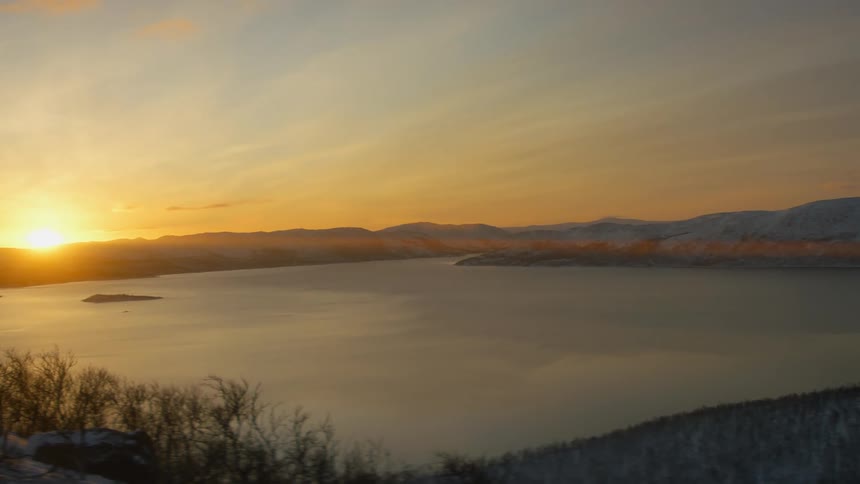 Sun rising over a mountain range in the distance with a large lake during the winter season