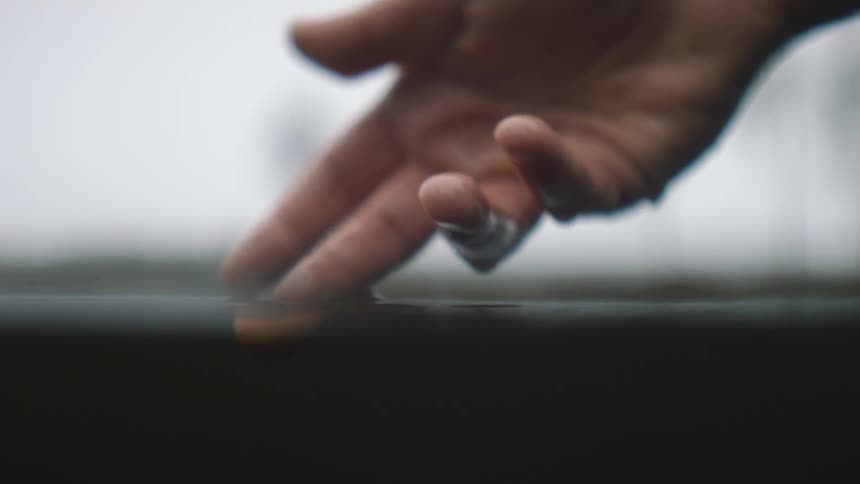 Person submerges fingers but not palm in water then raises hand to stroke along surface