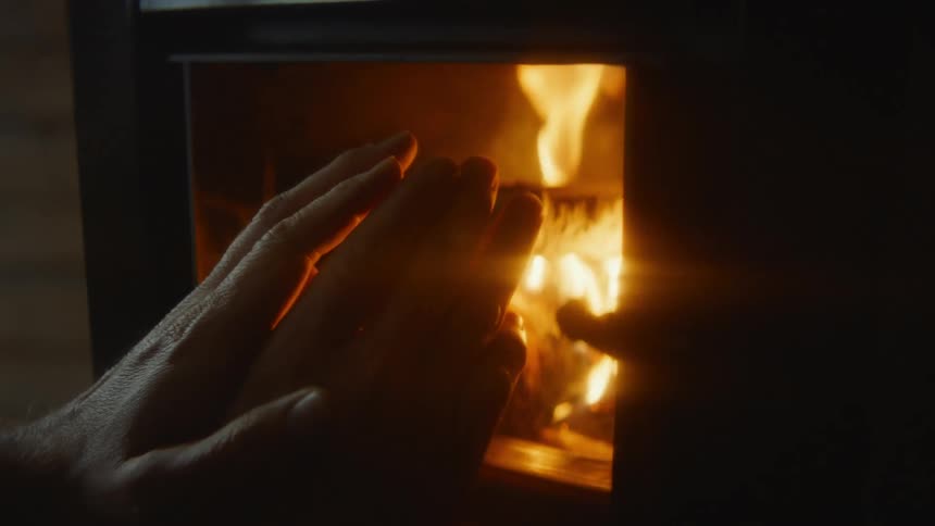 A person in a room holding out their hands with a fireplace fire and smoke in the background