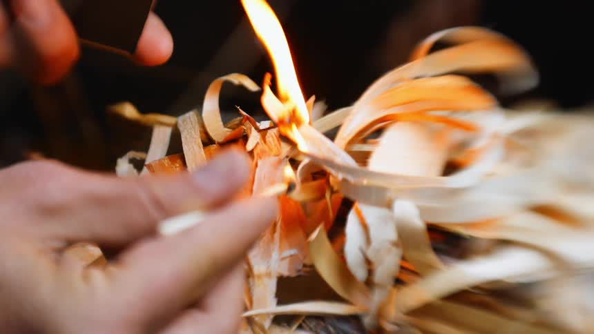 A man uses a match to light curly wood shavings on fire