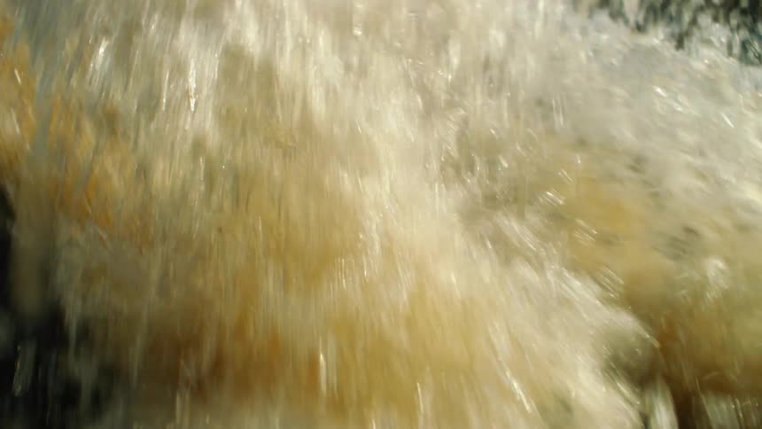 Water flows violently across rocks in a river during the day