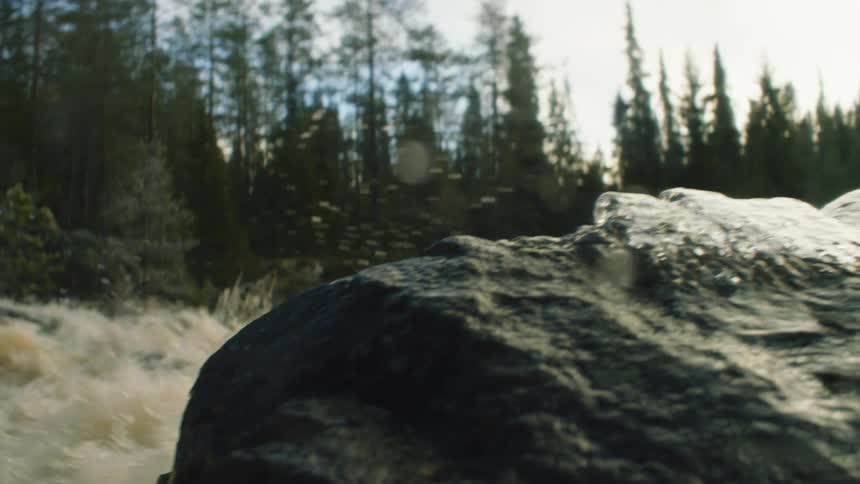 The rough river waters crash against the boulder