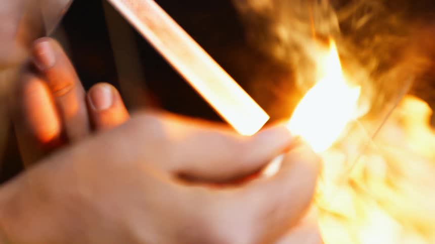 A person in a room lighting a match with smoke and fire on a matchbox