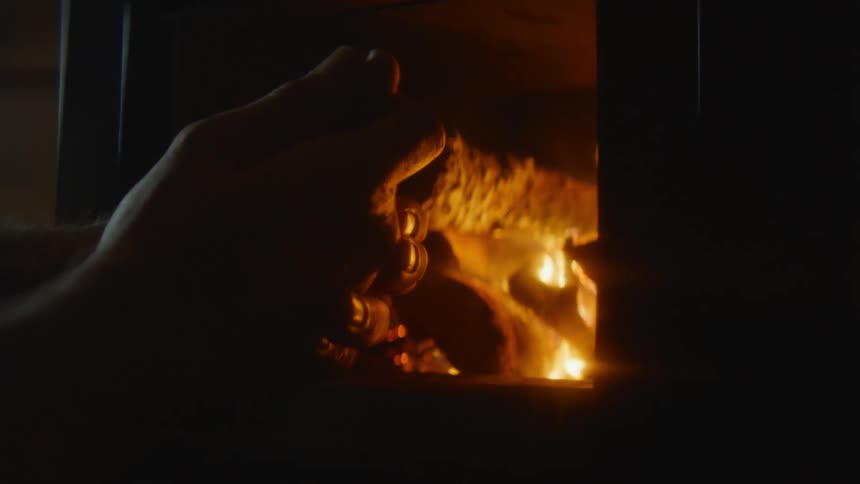 A man warms his hands in front of a burning wood stove