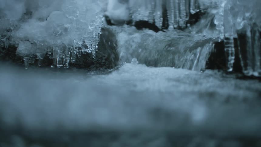 Water pouring down a small waterfall in a river surrounded by rocks covered in icicles and frost