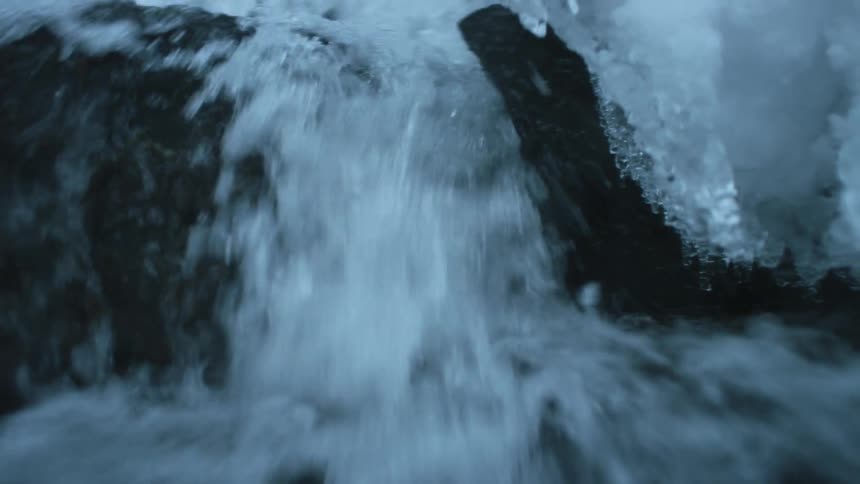 A stream of water pouring down from a small waterfall surrounded by icicles and snow