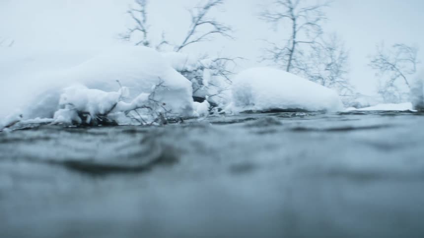 A river in a forest surrounded by rocks and vegetation covered and snow