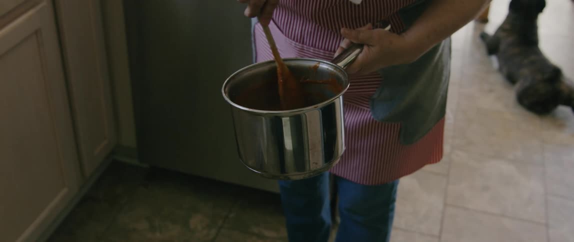 A woman stirring food in a stainless steel pot while standing in a kitchen