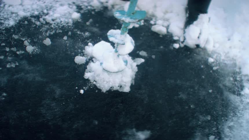 A person using a drill to drill a hole in ice water and snow
