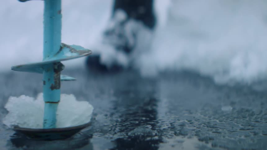 A person using a drill to open a hole on the frozen surface of a lake