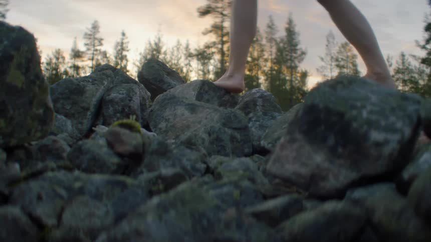 A person walking barefoot over boulders in a forest at sunset