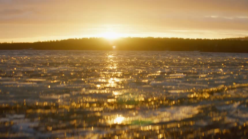 A lake with ice and water with trees the sky and clouds in the background
