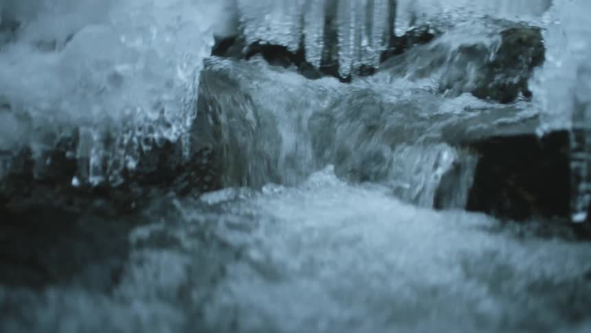 Rushing water flows between icicle and ice covered banks foaming and bubbling