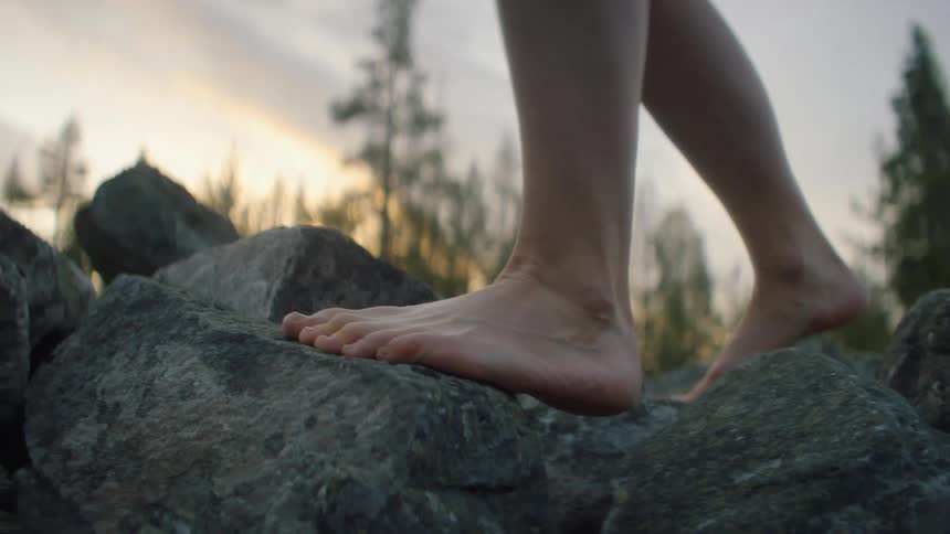 A barefooted person carefully takes steps across a group of uneven rocks